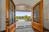 Arched double-entry natural wood doors with glass panels and matte black hardware, opening to a covered porch with a tongue-and-groove ceiling and pav