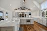 Vaulted ceiling with exposed timber beams, white shaker cabinetry, quartz surfaced countertops, apron-front farmhouse sinks, and wood-finish flooring