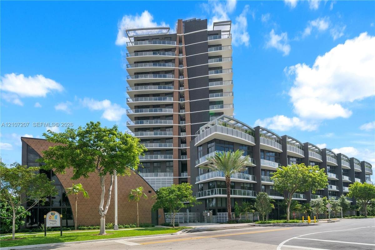 Contemporary high-rise architecture featuring glass-railed private balconies, a multi-story facade with dark paneling, and an attached low-rise struct