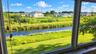 Expansive multi-pane window featuring water frontage, grassy landscape, and mature trees