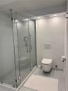 Frameless glass walk-in shower with stone-finish tiling, wall-mounted toilet, recessed ceiling lighting, and chrome fixtures