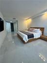 Large-format tile flooring, recessed ceiling lighting, and integrated wall-to-wall wood-finish headboard with matching side tables