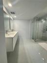 Floating dual-sink vanity with a solid-surface countertop, glass-enclosed shower, polished large-format floor tile, and rectangular wall-mounted mirro