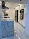 Modern kitchen featuring white flat-panel cabinetry, waterfall-edge stone-finish countertop, stainless steel built-in double oven, glass cooktop, and 