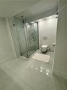 Glass-enclosed shower with polished chrome fixtures, large-format tile flooring, and wall-mounted toilet