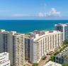 High-rise coastal development featuring white concrete facade, stacked private balconies, and expansive water frontage