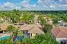 Aerial perspective featuring a tile roof, screened-in swimming pool, mature palm trees, and hardscaped driveway