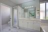 Bathroom featuring white cabinetry, solid-surface vanity countertop, full-width wall mirror, chrome-finish plumbing fixtures, and marble-patterned til
