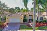 Stucco exterior featuring a tiled roof, multi-pane arched windows, a paved driveway, and mature palm trees
