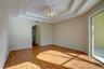Room featuring a multi-tiered tray ceiling, wood-finish flooring, a central ceiling fan with multi-light fixture, an arched entryway, and a sliding gl