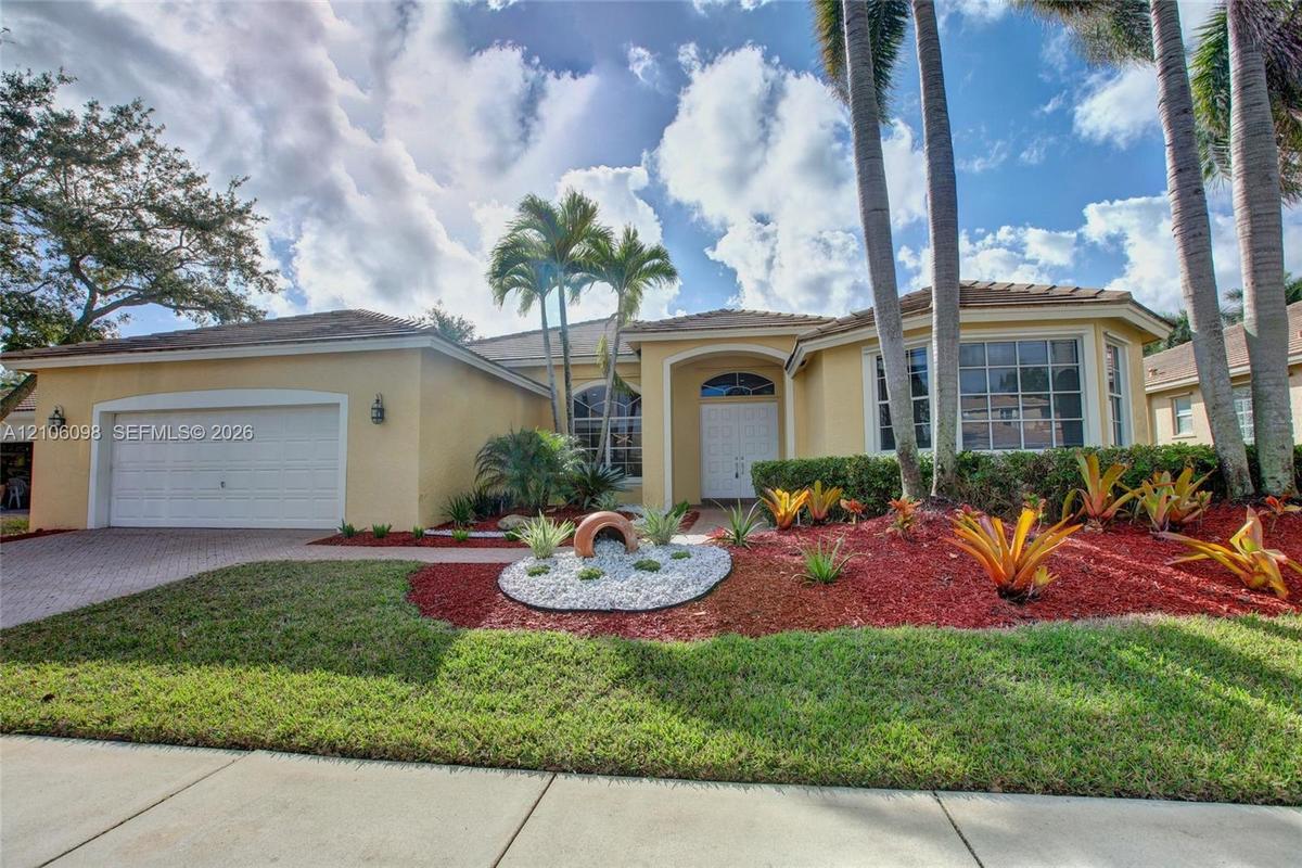 Single-story residence featuring a stucco exterior, multi-pane windows, a paver driveway, an attached two-car garage, and established tropical landsca