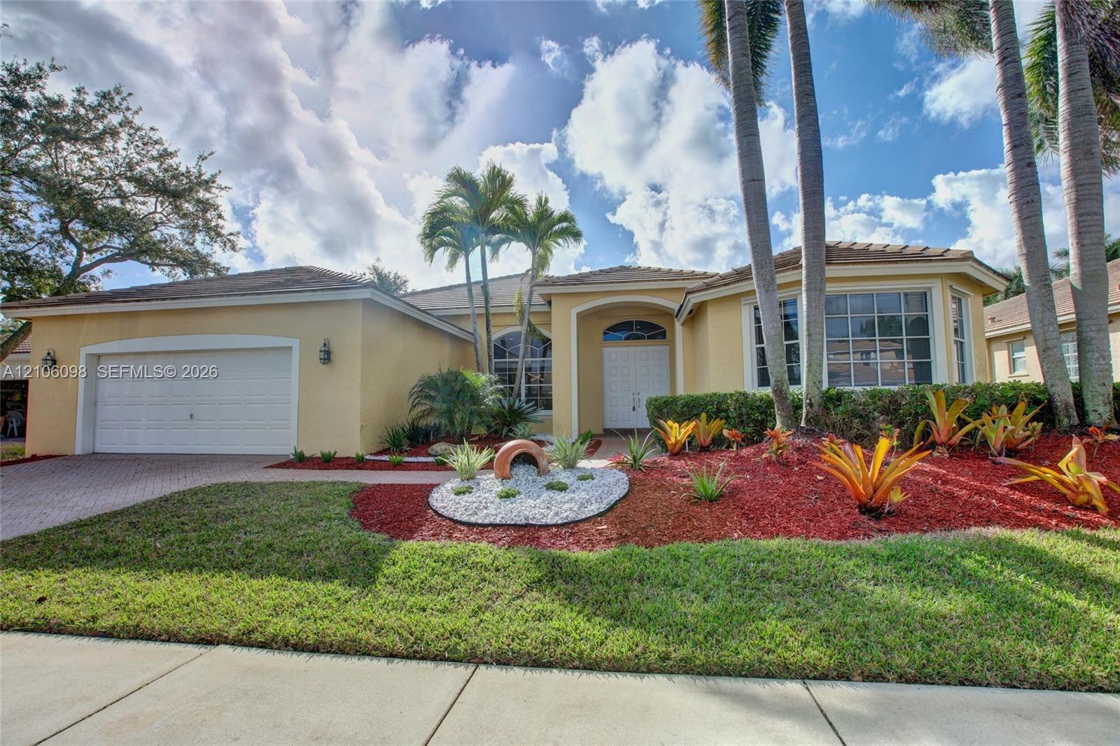 Single-story residence featuring a stucco exterior, multi-pane windows, a paver driveway, an attached two-car garage, and established tropical landsca
