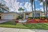 Single-story residence featuring a stucco exterior, multi-pane windows, a paver driveway, an attached two-car garage, and established tropical landsca