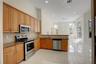 Kitchen featuring natural wood cabinetry, stone countertops, stainless steel appliances, recessed lighting, and large-format tile flooring