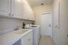 Utility area featuring white shaker-style wall cabinetry, a composite utility sink with a chrome faucet, solid-surface countertops, and tile flooring