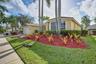 Single-story exterior featuring a stucco facade, multi-pane bay window, attached garage, and landscaped garden beds with palm trees