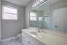 Bathroom featuring a solid-surface countertop with an integrated basin, white shaker-style vanity cabinetry, a full-width wall mirror, a multi-bulb li