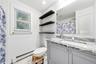 Bathroom featuring a gray vanity with stone countertop, undermount sink, wall-to-wall mirror, built-in open shelving, and a tiled shower surround