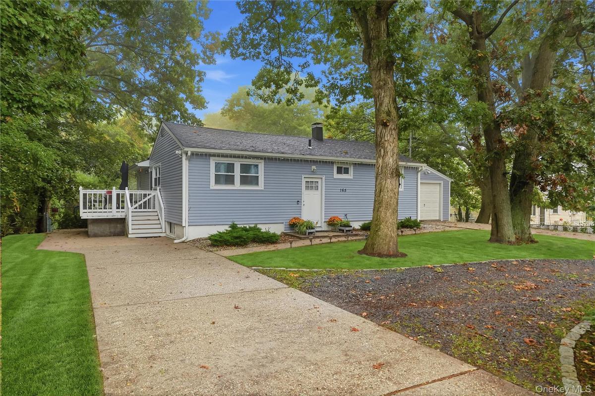 Exterior featuring light blue horizontal siding, white trim, a detached garage, a raised deck with stairs, and a concrete driveway