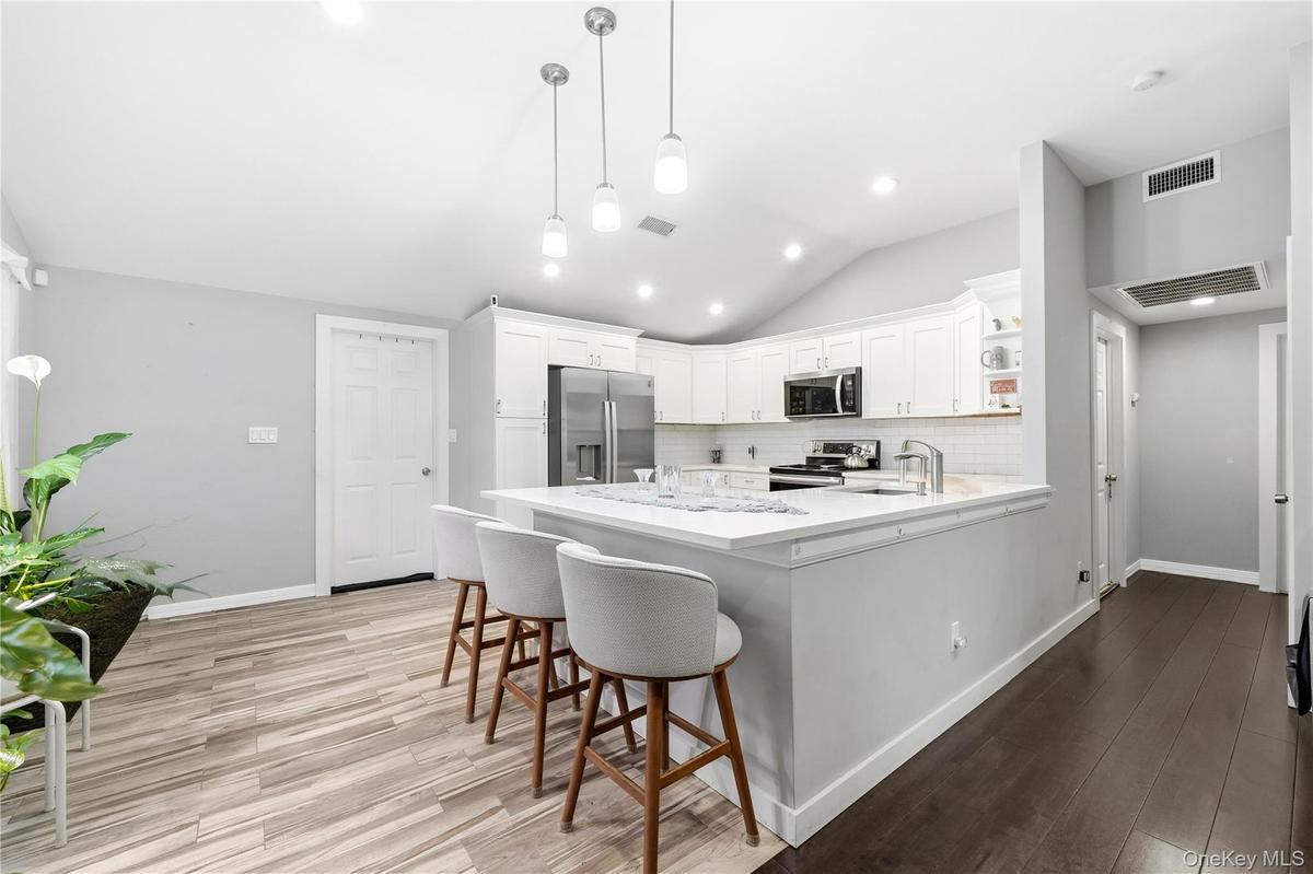 Kitchen featuring white shaker-style cabinetry, white countertops, stainless steel appliances, pendant lighting, and wood-finish flooring