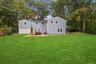 Expansive backyard featuring a manicured lawn, perimeter fencing, gravel patio area, and mature trees