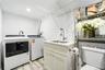 Laundry area featuring wood-finish flooring, white Shaker-style cabinetry, an integrated utility sink with a high-arc pull-down faucet, and overhead w