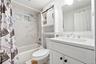 Bathroom featuring a vanity with a white countertop and rectangular undermount sink, large wall-mounted mirror, white built-in storage cabinet with sl