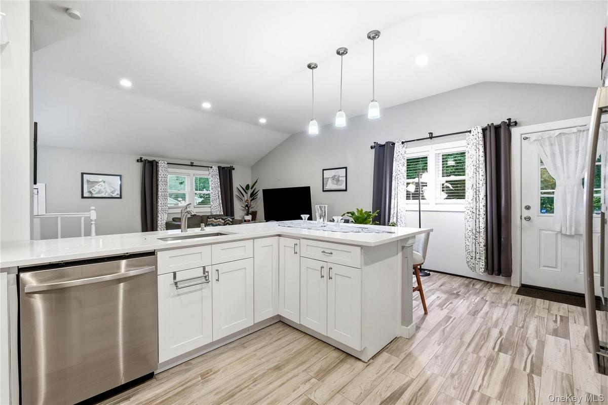 Kitchen featuring white shaker-style cabinetry, white countertops, stainless steel undermount sink, pendant lighting, and wood-finish flooring under a