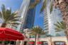 High-rise glass facade featuring wraparound balconies, decorative stone-finish exterior walls, and manicured palm trees