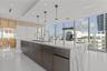 Kitchen featuring a waterfall-edge island with stone countertop, flat-panel cabinetry, dual gooseneck faucets, glass pendant lighting, and floor-to-ce
