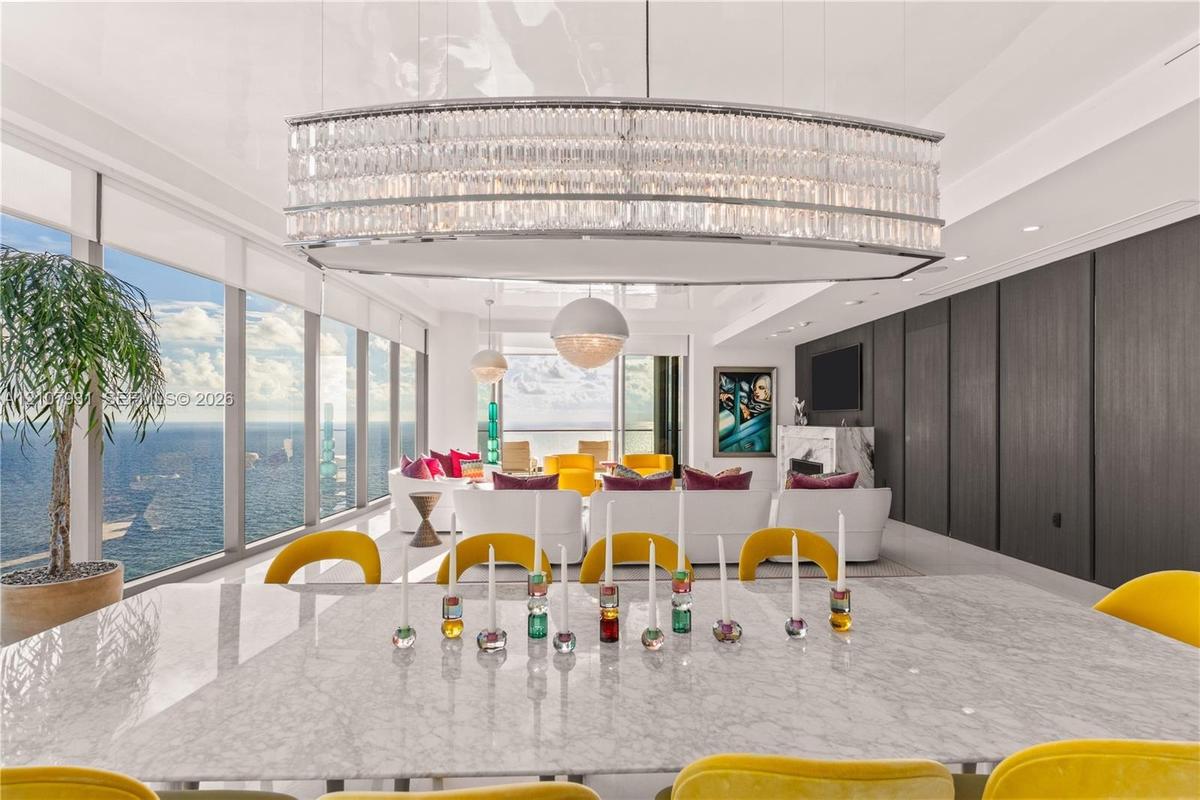 Expansive living area featuring floor-to-ceiling windows, an elongated crystal chandelier, high-gloss ceiling finish, and built-in dark wood-panel wal