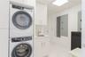 Laundry room featuring a stacked appliance set, white cabinetry, a built-in sink with a chrome faucet, and tile flooring