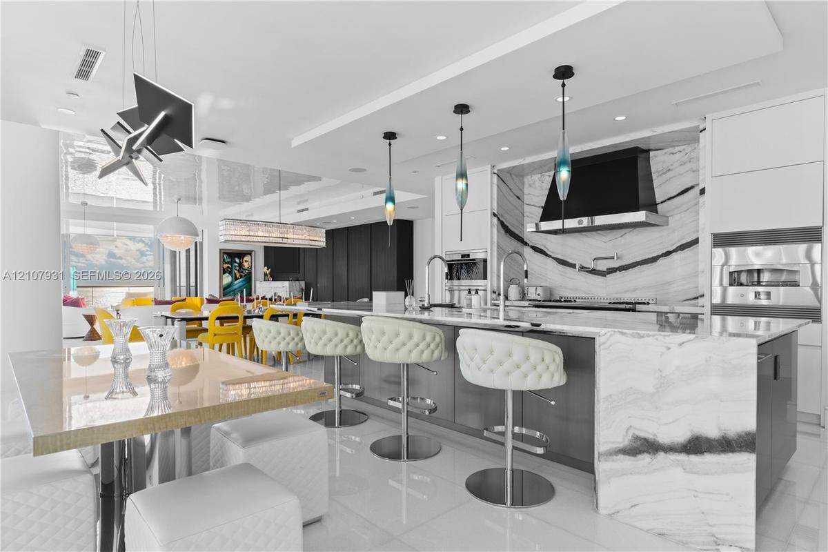 Contemporary kitchen featuring a stone-topped waterfall island, custom cabinetry, a slab backsplash, integrated wall oven, and pendant lighting