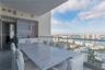 Covered balcony featuring an integrated outdoor kitchen with white cabinetry, horizontal tile wall accent, glass railing, and expansive water and city