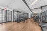 Fitness area featuring wood-finish flooring, floor-to-ceiling black-and-white stone wall cladding, a textured geometric ceiling, and double-paned glas