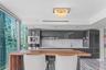 Contemporary kitchen featuring high-gloss cabinetry, stone backsplash, integrated stainless steel coffee system, wood-finish breakfast bar, and polish