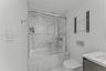 Bathroom featuring a tub-shower combination with glass sliding doors, floor-to-ceiling stone-look tiling, a wall-mounted toilet with a dual-flush actu