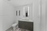 Wall-mounted vanity with a rectangular vessel sink and countertop, backlit rectangular mirror, and glass wall shelving
