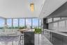 Kitchen featuring high-gloss cabinetry, stone countertops, integrated appliances, floor-to-ceiling windows, and polished stone flooring