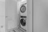Laundry closet featuring a stacked front-load washer and dryer and a louvered door