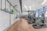 Fitness center featuring wood-finish flooring, sculptural geometric ceiling panels, linear recessed lighting, floor-to-ceiling windows, and wall-mount