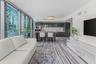 Floor-to-ceiling windows, high-gloss cabinetry, stone-patterned tile flooring, integrated kitchen appliances, and a kitchen island with a wood-finish 