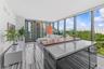Floor-to-ceiling windows, kitchen island with stone countertop and raised wood-finish bar, and light-toned tile flooring