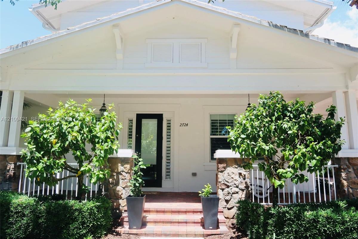 Covered front porch featuring a stone veneer base, white balustrades, brick-paver steps, and a glass-paneled entry door