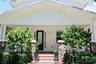 Covered front porch featuring a stone veneer base, white balustrades, brick-paver steps, and a glass-paneled entry door