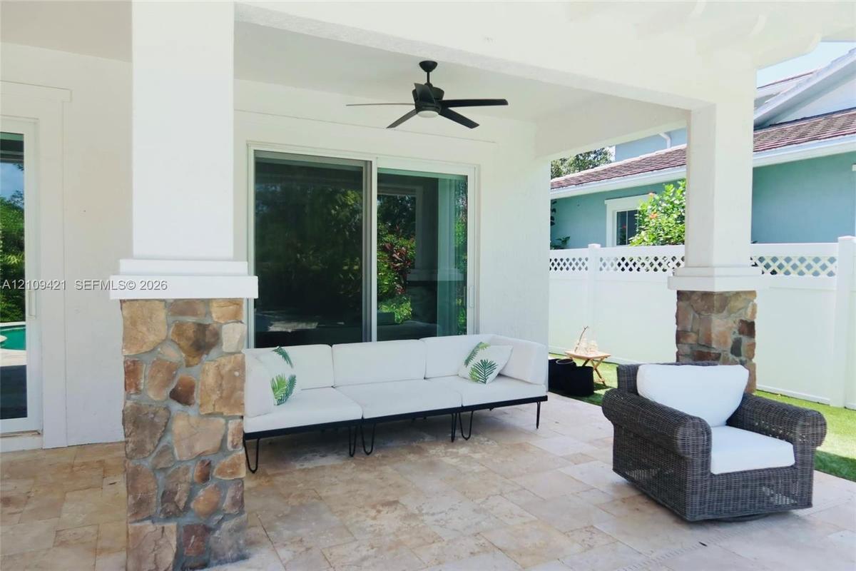 Covered patio featuring stone-clad pillars, natural stone flooring, and a ceiling-mounted fan