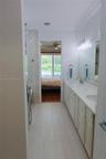Bathroom featuring dual-sink vanity with light-tone cabinetry, quartz countertop, full-width wall mirror, and large-format tile flooring