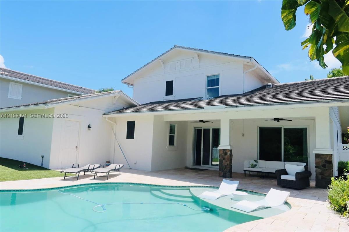 Swimming pool with a baja shelf, covered patio with ceiling fans, stone-pillar accents, and exterior light fixtures