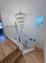 Multi-level staircase featuring wood-finish flooring, a white painted wood railing with detailed balusters, and a tiered brass candelabra chandelier
