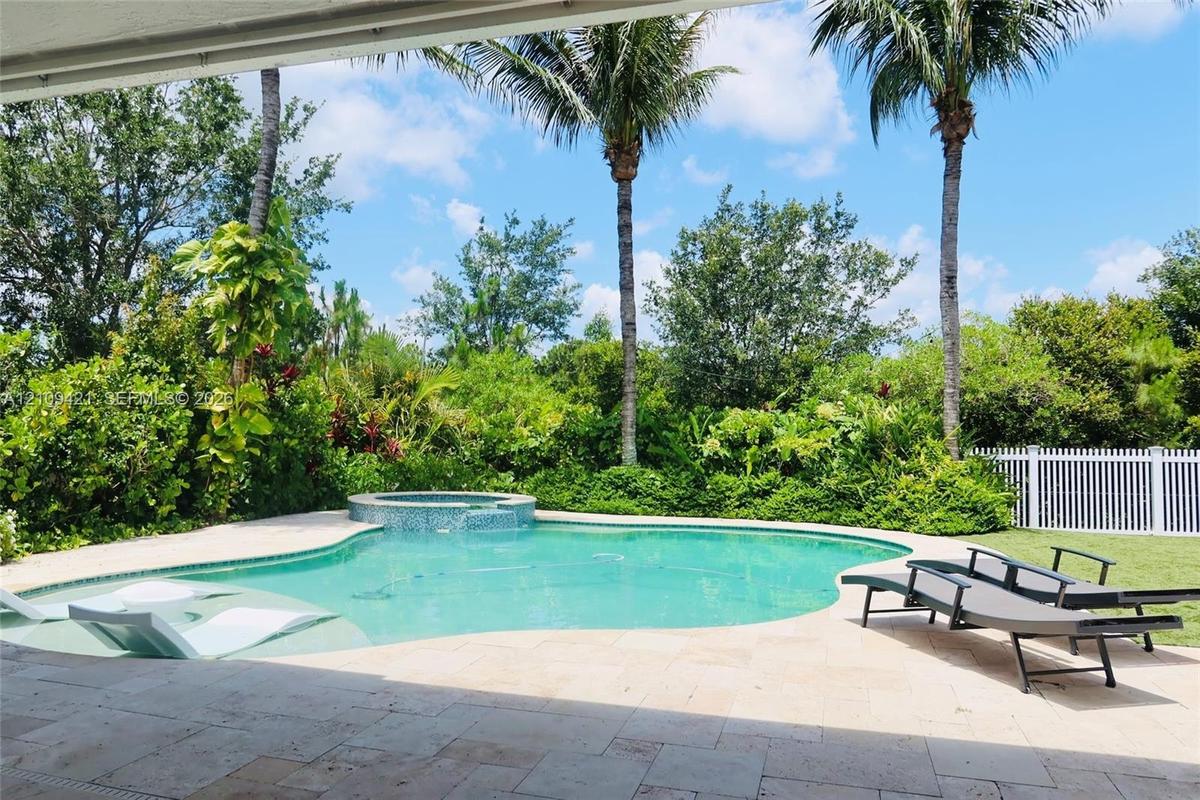 Backyard swimming pool with an integrated spa, tiled pool deck, palm trees, and perimeter fencing